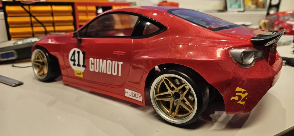 Punainen RC-drift-auto takaviistosta, takasiipi ja Gumout 411 -teippaus