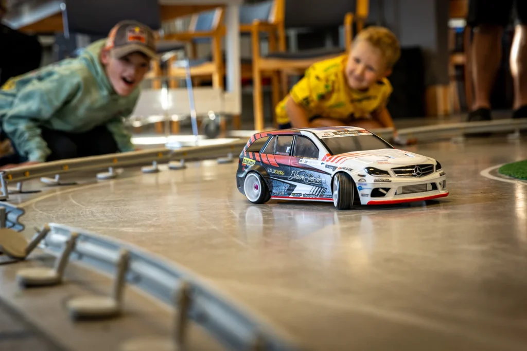 Aikuinen ja lapsi seuraamassa RC-drift-autoa radan vieressä kerhoillassa