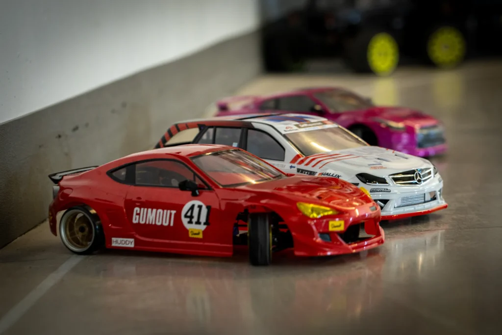 Kolme RC-drift-autoa rivissä radalla: punainen, valkoinen ja pinkki kori