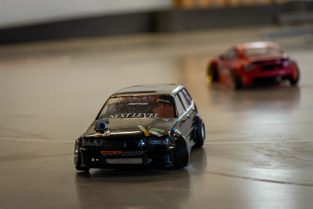 Musta RC-drift-auto kaarteessa, taustalla punainen auto